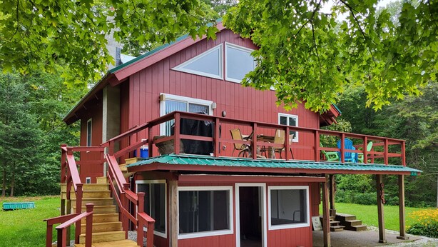 A two-story house with a red exterior, a balcony with chairs, and a wooden staircase leading to the entrance. - Hike, ski, summer fun in our all season home minutes to Okemo. Dogs welcome! (Mt Holly)