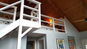 A multi-level wooden interior with a staircase, a ceiling fan, and two framed posters on the wall. - Hike, ski, summer fun in our all season home minutes to Okemo. Dogs welcome! (Mt Holly)