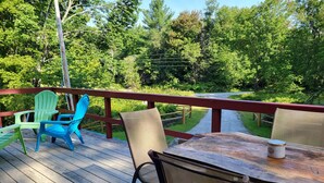 A wooden deck with a table and chairs, overlooking a river and surrounded by greenery. - Hike, ski, summer fun in our all season home minutes to Okemo. Dogs welcome! (Mt Holly)