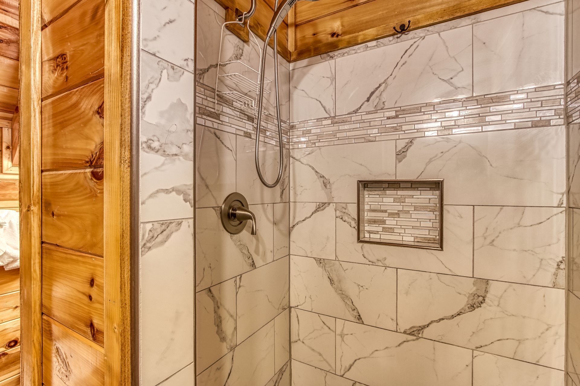 A shower with a marble wall, a wooden ceiling, and a small framed tile design.