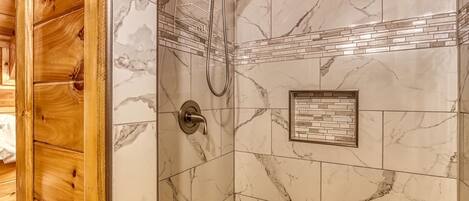 A shower with a marble wall, a wooden ceiling, and a small framed tile design.