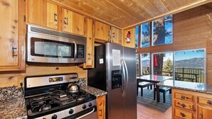 A kitchen with wooden cabinets, a stainless steel stove, a microwave, and a refrigerator. There is a window with a view of trees and mountains.