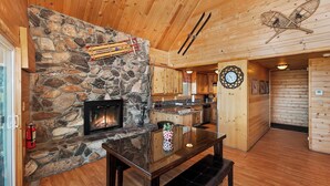 Un intérieur de chalet chaleureux avec une cheminée en pierre, des murs en bois, un coin repas et une cuisine.