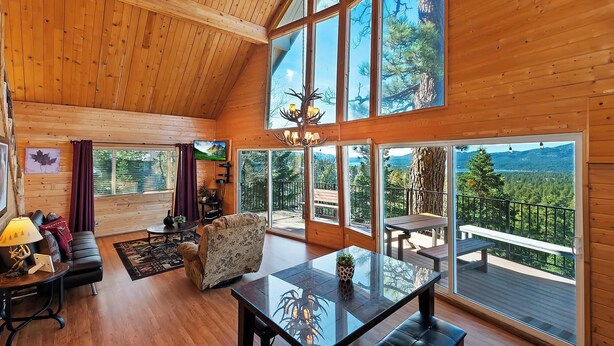 A spacious cabin with a high ceiling, large windows offering mountain views, a cozy seating area, and a dining table.