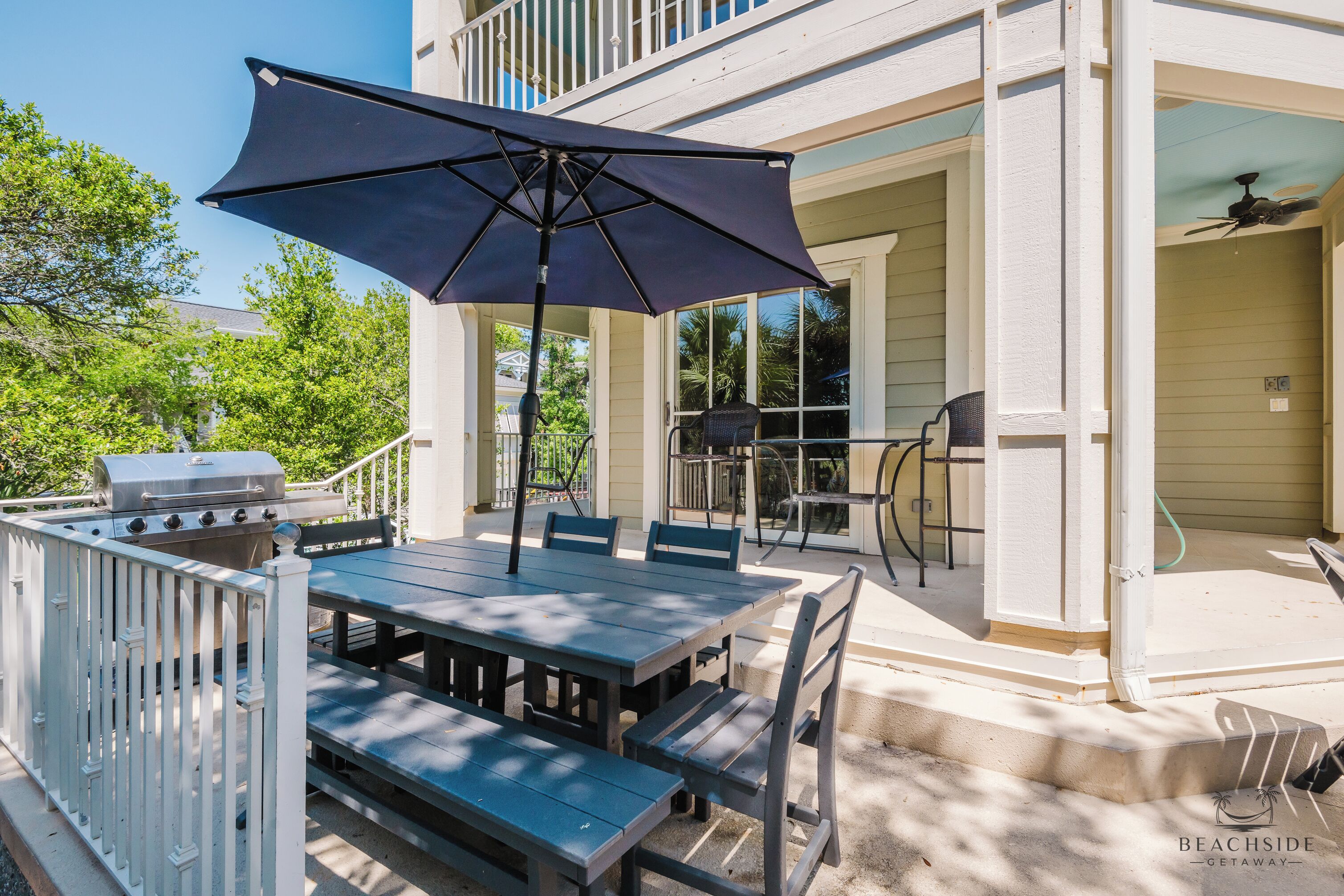 An outdoor patio with a table and chairs, a grill, and a covered umbrella.