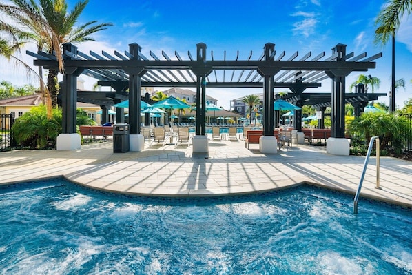 A pool area with a pergola, lounge chairs, and umbrellas.