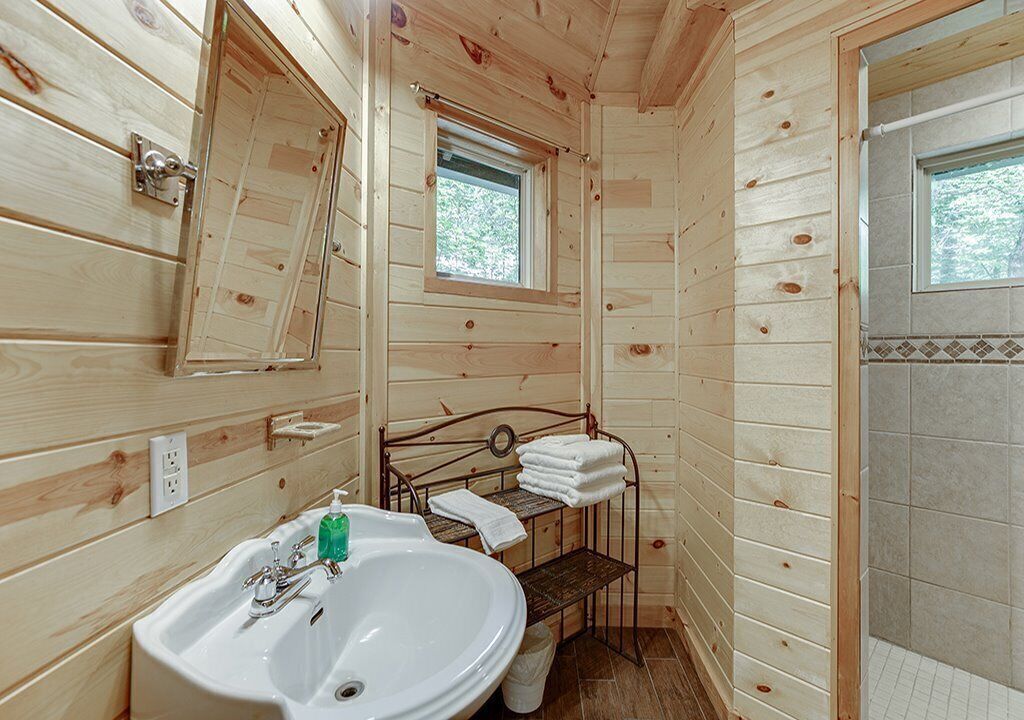 Baño de una cabaña de madera con lavamanos, espejo y ducha.
