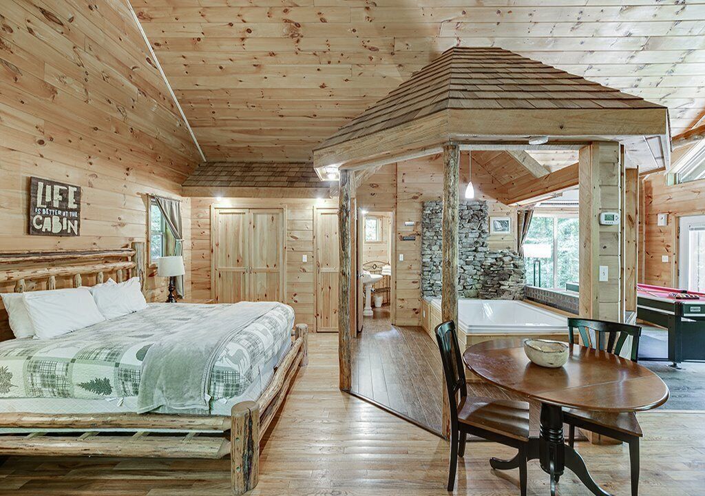 Interior de una cabaña con una cama de madera, una mesa de comedor y una chimenea de piedra.