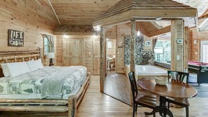 Interior de una cabaña con una cama de madera, una mesa de comedor y una chimenea de piedra.