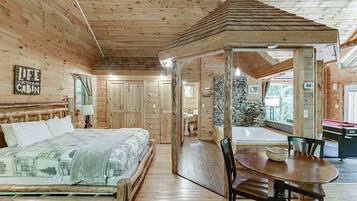 Interior de una cabaña con una cama de madera, una mesa de comedor y una chimenea de piedra.