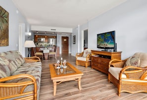 A living room with wicker furniture, a wooden coffee table, and a television on a wooden cabinet.