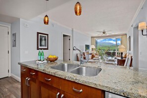 A kitchen with granite countertops, stainless steel sinks, wooden cabinets, and pendant lighting.