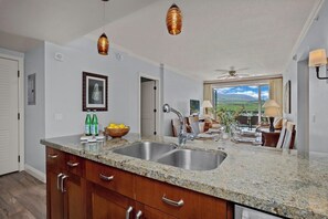 A kitchen with granite countertops, stainless steel sinks, wooden cabinets, and pendant lighting.
