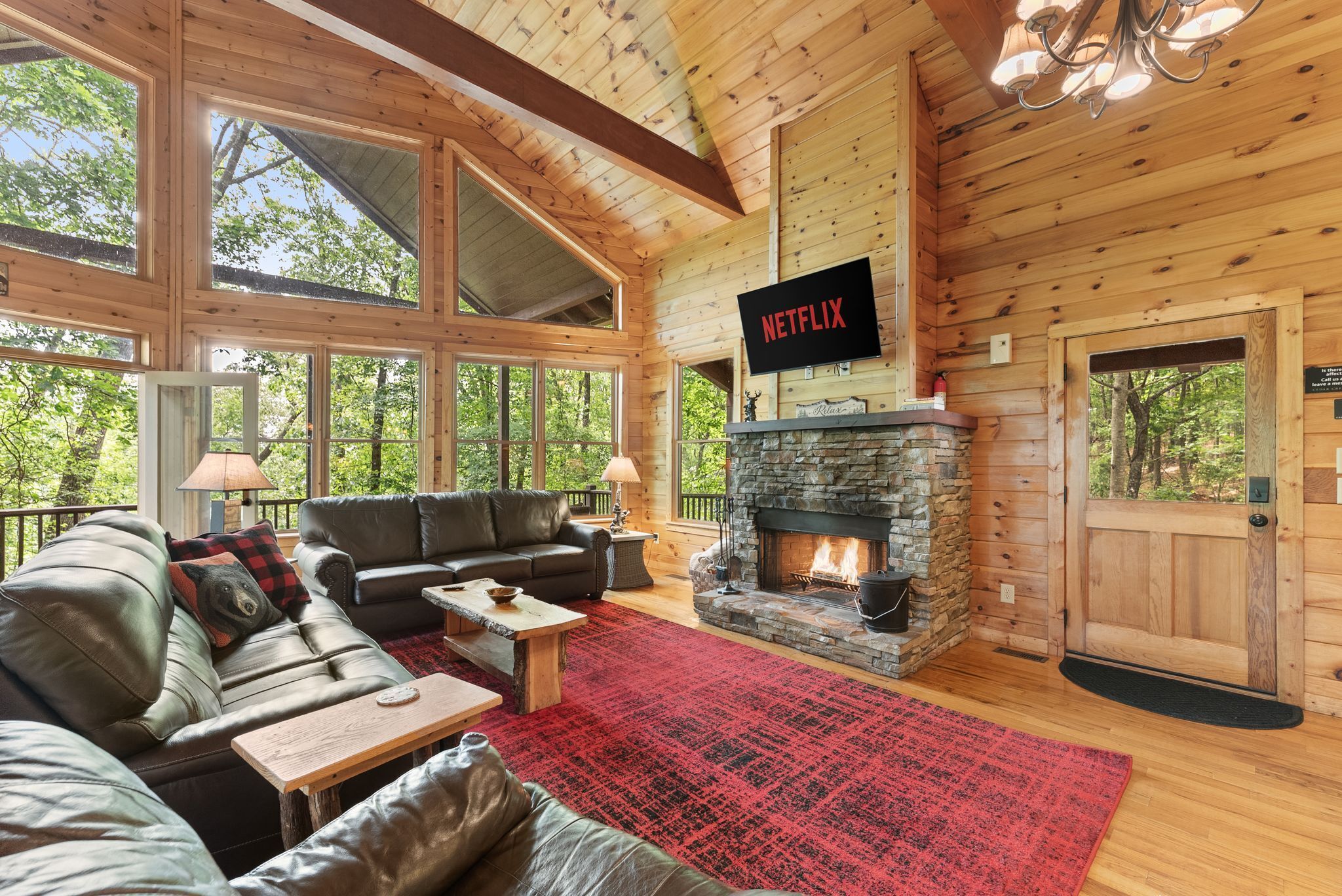 L’intérieur d’une cabane en rondins, avec une cheminée en pierre, des canapés en cuir, un tapis rouge et un logo Netflix.