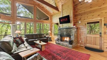 L’intérieur d’une cabane en rondins, avec une cheminée en pierre, des canapés en cuir, un tapis rouge et un logo Netflix.