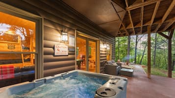 Un bain à remous à l’extérieur d’un chalet, avec un panneau d’avertissement, une terrasse en bois et des sièges d’extérieur.