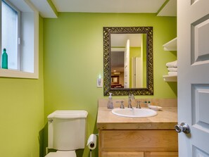 Casa de banho com uma parede verde, sanita branca, lavatório com espelho e porta com um porta-toalhas.