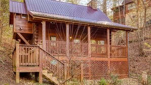 A wooden cabin with a metal roof, a wooden deck, and a staircase leading to a porch.