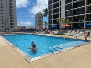 Una piscina con sillones de playa y sombrillas, rodeada de edificios altos.