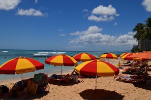 Een strand met meerdere rode en gele gestreepte parasols, strandstoelen en een helder uitzicht op de oceaan.