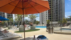 A poolside area with lounge chairs, umbrellas, and a pool. - Waikiki Banyan 1909 Amazing Views and Just  Steps to the Beach (Honolulu)