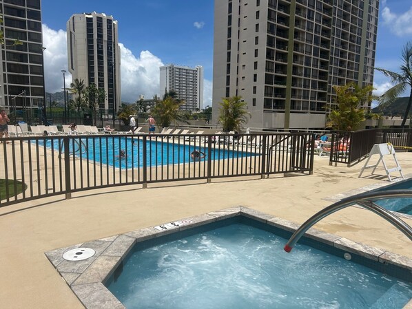 Zona de piscina con un deck cercado, sillas de descanso y un jacuzzi.