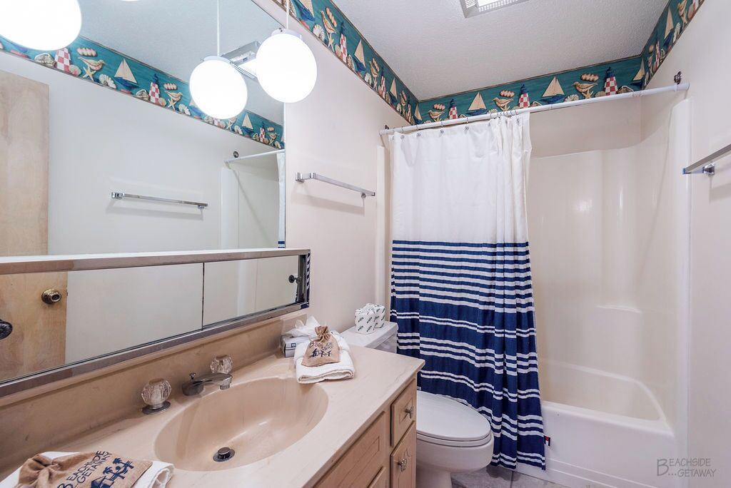 A bathroom with a sink, mirror, and a shower with a striped curtain.