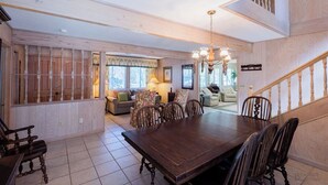 A spacious dining area with a large wooden table and chairs, a chandelier, and a staircase leading to an upper level. - 2 Bayberry - 4th Row Home, Short Walk to Beach! (Hilton Head Island)
