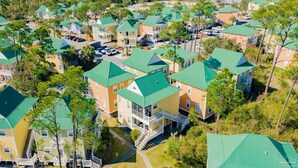 Um bairro residencial com várias casas de dois andares, com telhados verdes e varandas, cercado por árvores.