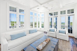 Un salon lumineux et spacieux, avec des meubles blancs, de grandes fenêtres et une vue sur la verdure.