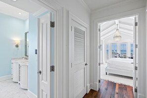 A bedroom with a large bed, a view of the ocean, and a bathroom with a vanity and mirror. - Beachfront with Pool and Golf Cart (Watersound)