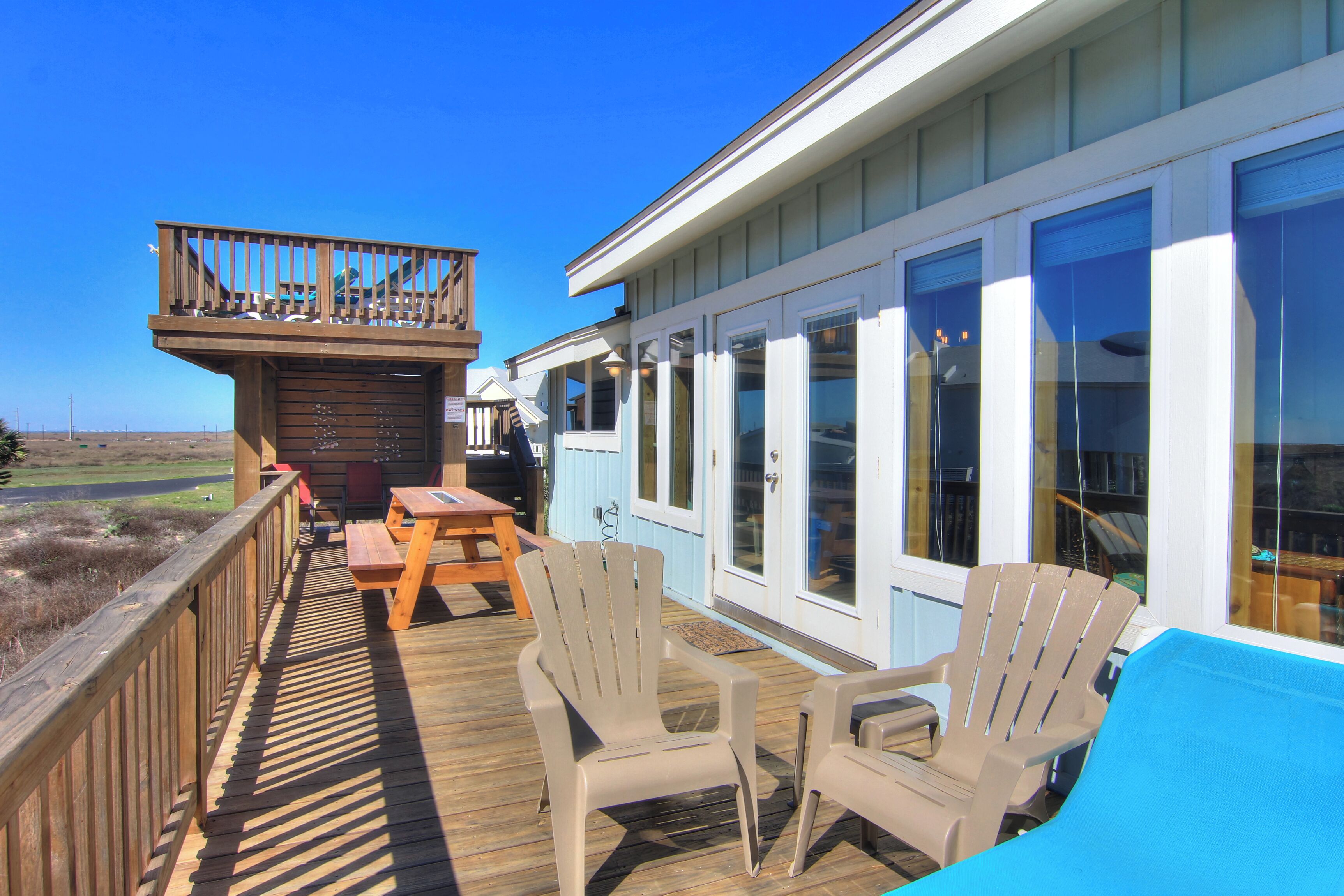 Une terrasse en bois avec des meubles d’extérieur et un espace abrité doté de grandes fenêtres.