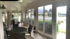 Une pièce lumineuse, baignée de soleil, avec une grande porte-fenêtre coulissante, un ventilateur de plafond et une table à manger avec des chaises.