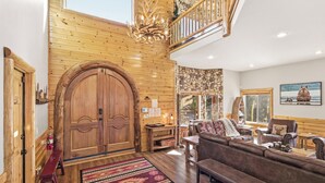 A spacious living area with a large wooden door, a chandelier, and a cozy seating arrangement.