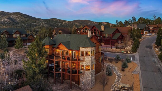 A multi-story lodge with a stone tower, wooden cabins, and a view of mountains.