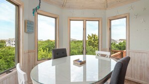 A round glass table with chairs in a room with wooden walls and large windows. - Pelican Shores: Private pool, 4 bedrooms, Whalehead Beach (Corolla)