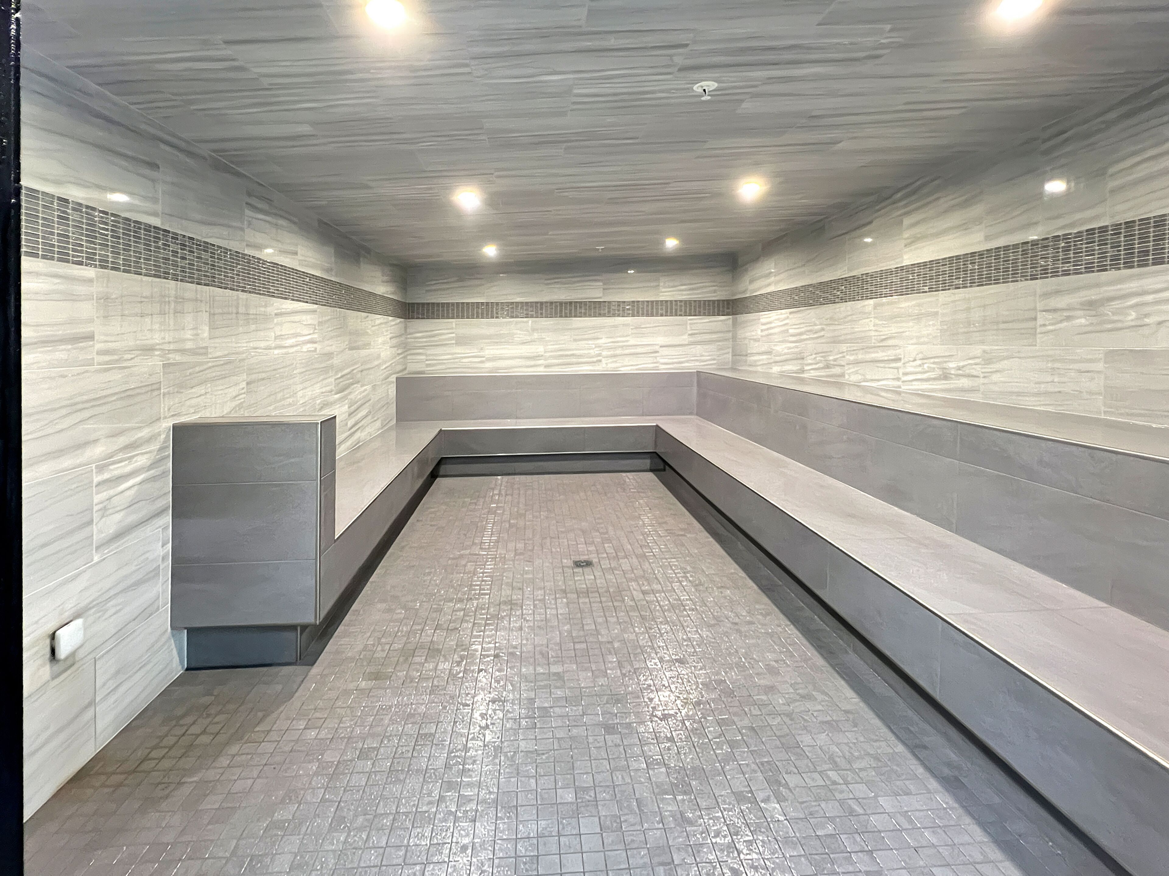 Un baño moderno con distribución rectangular, paredes y piso cubiertos de azulejos.