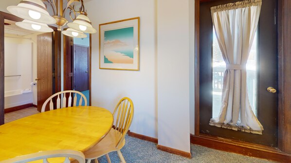 A dining area with a wooden table and chairs, a painting on the wall, and a door with curtains. - Mountain Green Ski & Golf Resort 2-E6 Across the Street from the Lifts (Killington)