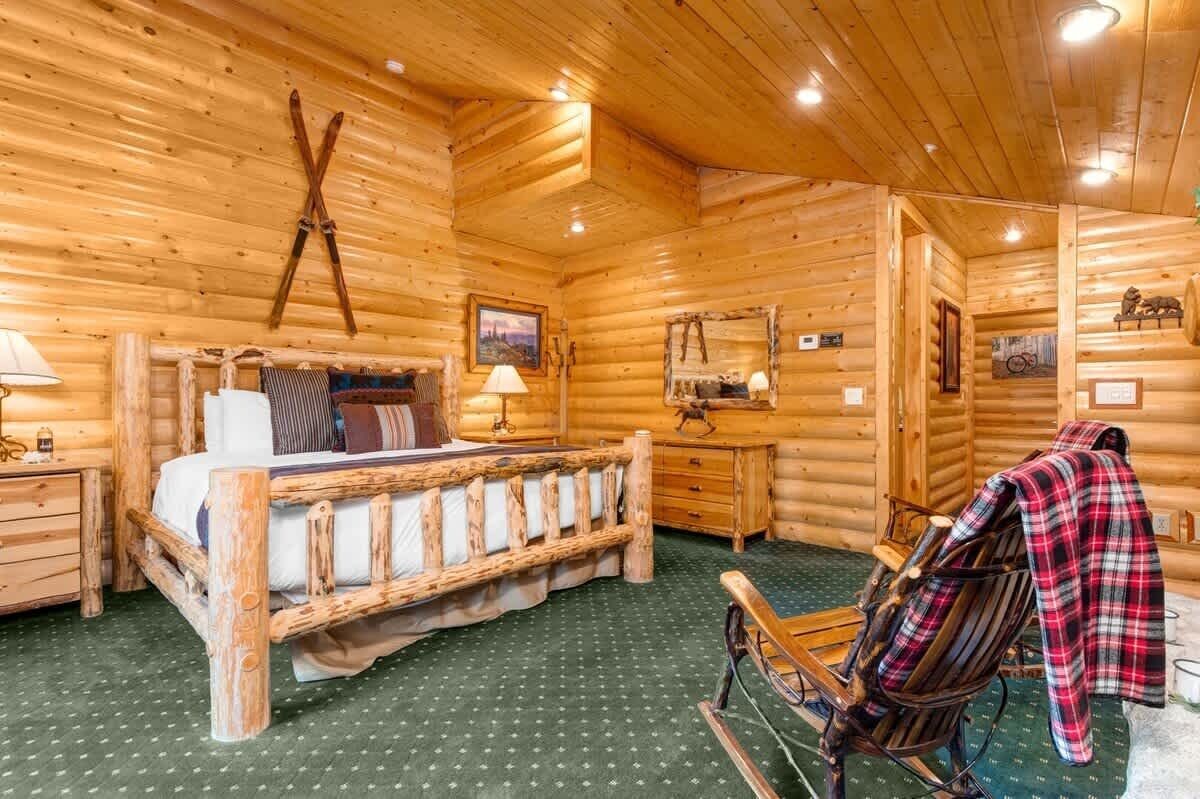 A log cabin interior with a wooden bed, a rocking chair, a wooden dresser, and a ski rack.