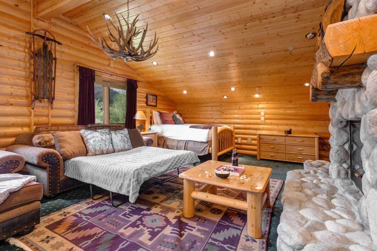 A log cabin interior with a bed, sofa, and coffee table, featuring wooden walls and a stone accent wall.