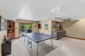 A spacious room with a ping pong table, a wooden cabinet, and a large window.