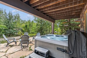 Zona de hidromasaje al aire libre con dos sillas Adirondack, un patio de piedra y una pérgola de madera.