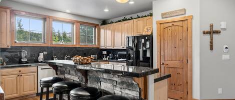 A kitchen with a central island, bar stools, wooden cabinets, a stone accent wall, and a cross on the wall.