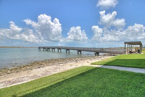 Un muelle se adentra en aguas tranquilas, un área con césped y un pabellón, bajo un cielo despejado.