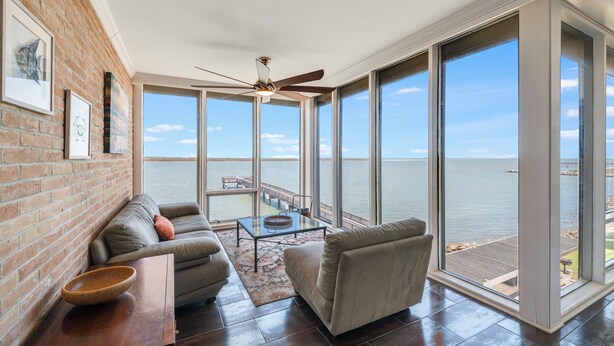 Ein geräumiges Zimmer mit großem Fenster mit Blick aufs Wasser, Deckenventilator, Sofa und Couchtisch.
