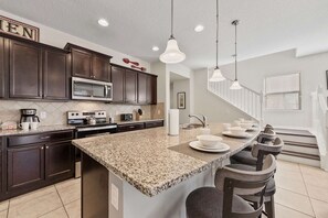 A kitchen with dark wood cabinets, a granite countertop, a stainless steel microwave, and a large island with bar stools.