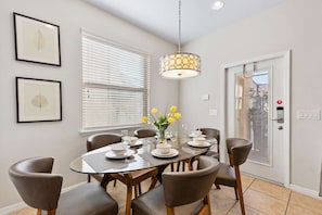 A dining area with a glass table, six chairs, a vase with yellow flowers, and a hanging light fixture. - Lake Access: 5BR Pool Townhouse near WDW (Kissimmee)