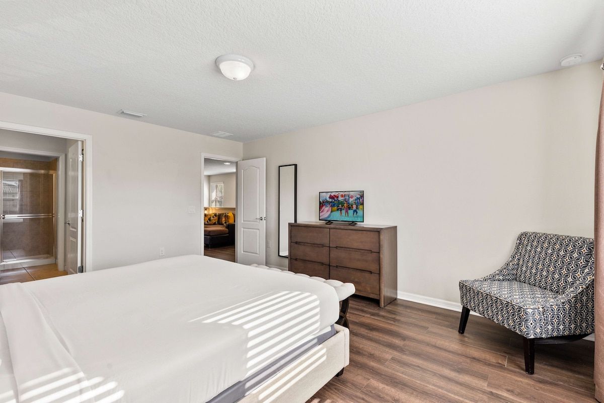 Een slaapkamer met een bed, een dressoir, een stoel en een televisie.