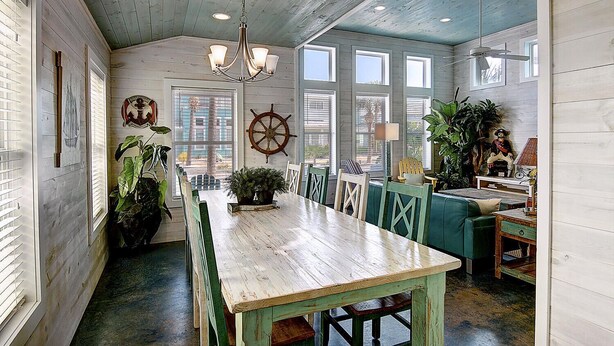 A nautical-themed dining area with a wooden table, chairs, and a ship's wheel decoration.