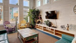 A cozy living room with wooden walls, a television mounted on the wall, and a variety of seating options including a couch, chairs, and a coffee table.